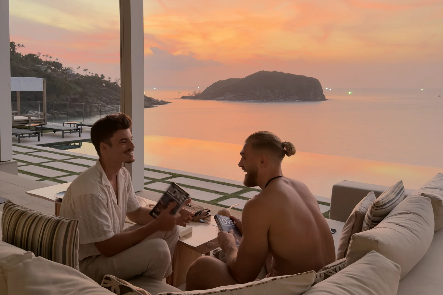 Zwei Männer im Gespräch auf einer Terrasse über dem Meer, Sonnenuntergang